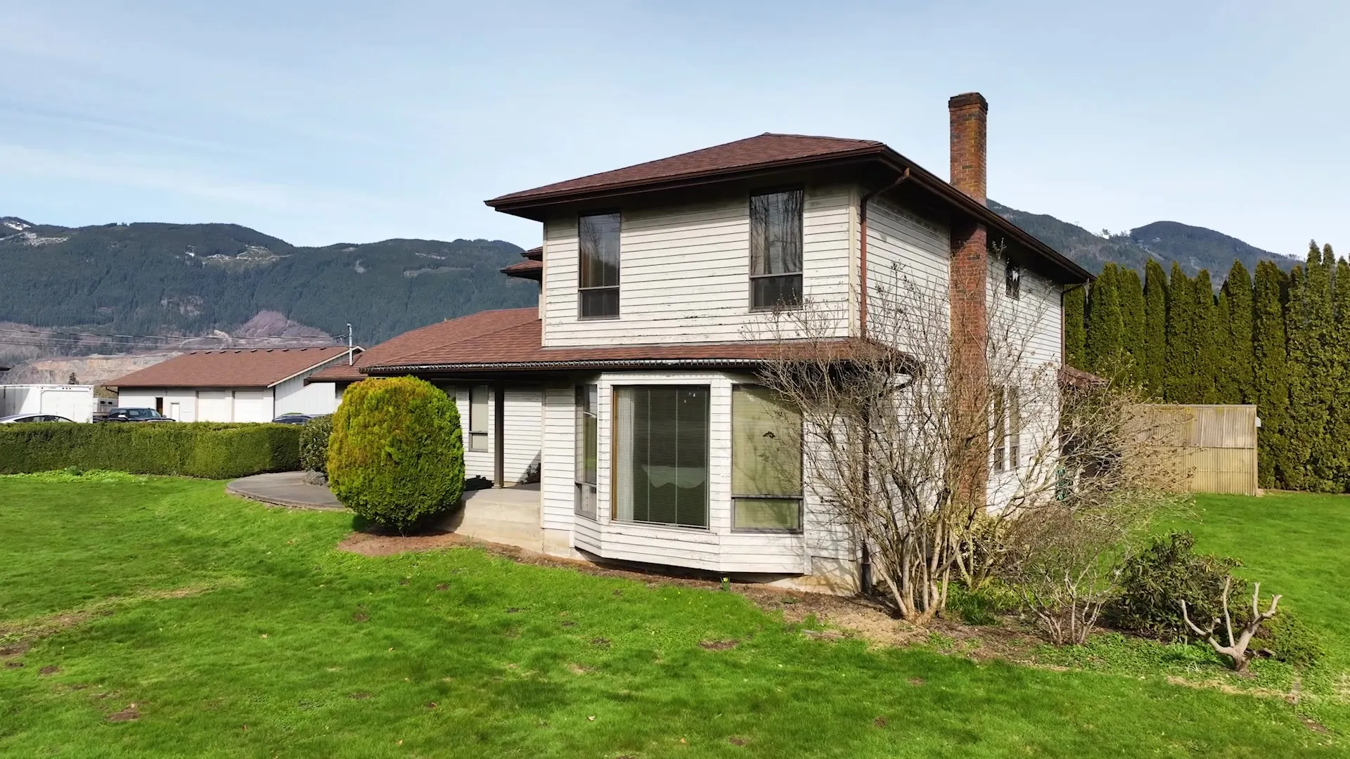 The home before, with tan siding, dark trim, and a brown roof looking dated from the street