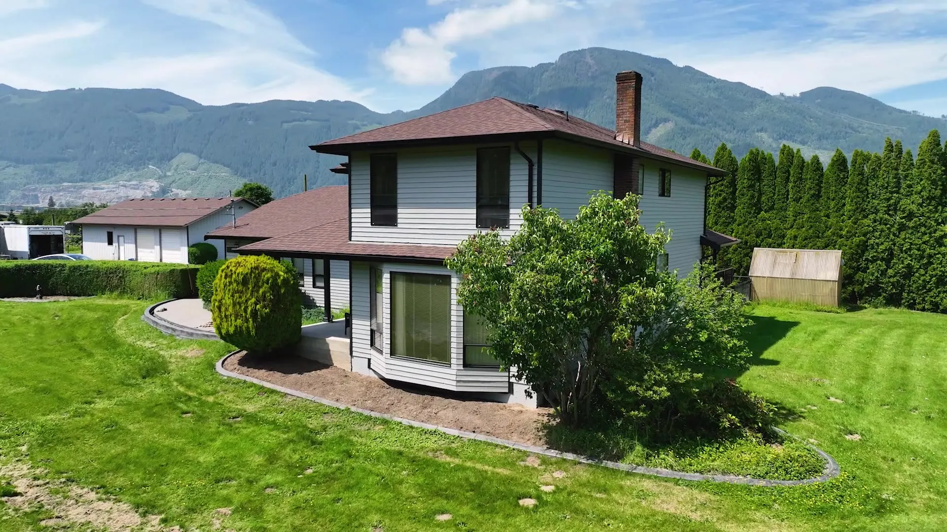 The same home after, with crisp light-grey siding and clean trim, framed by mountains