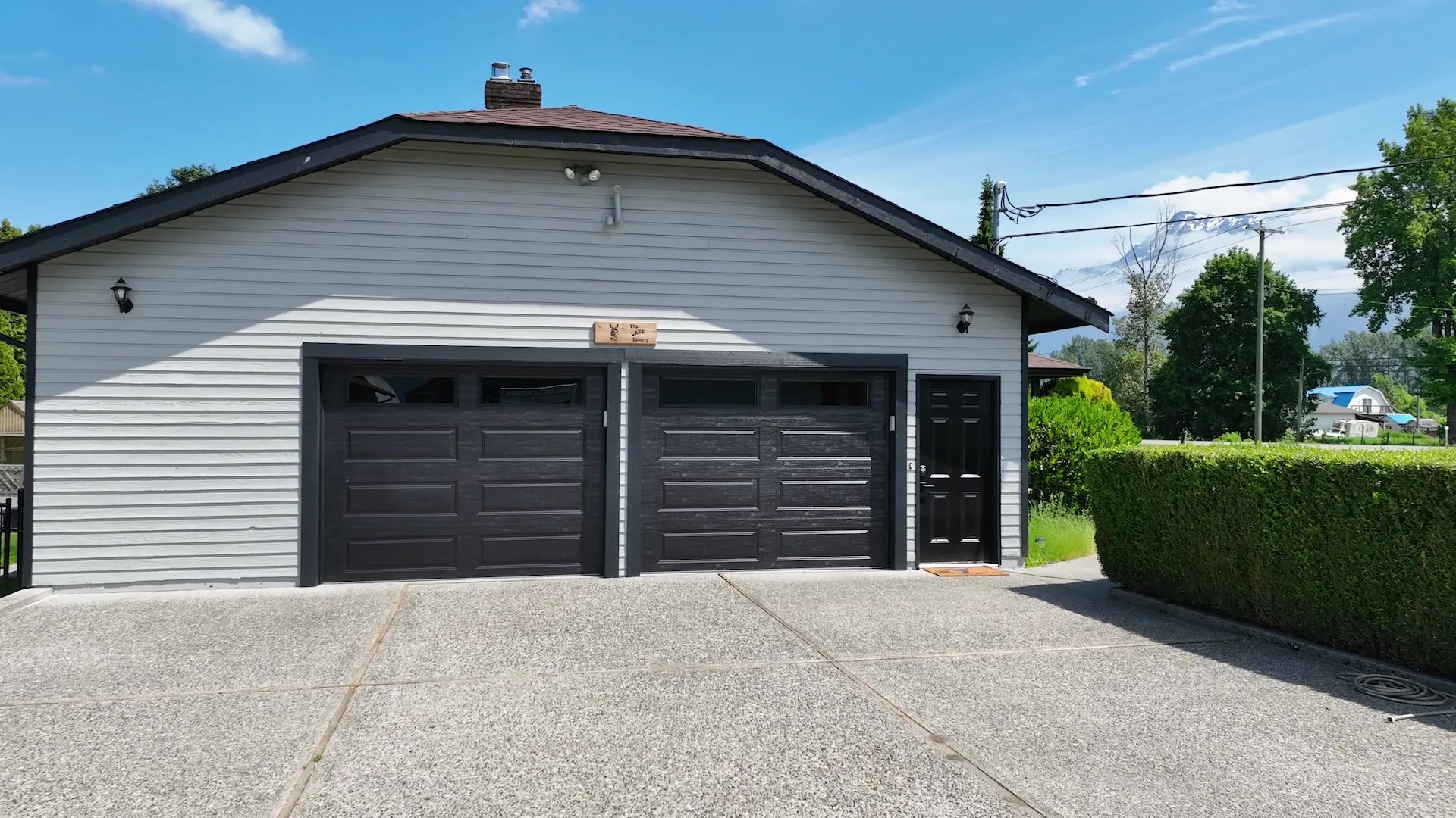 Renovated home exterior with light-grey siding and bold black garage doors under a blue sky