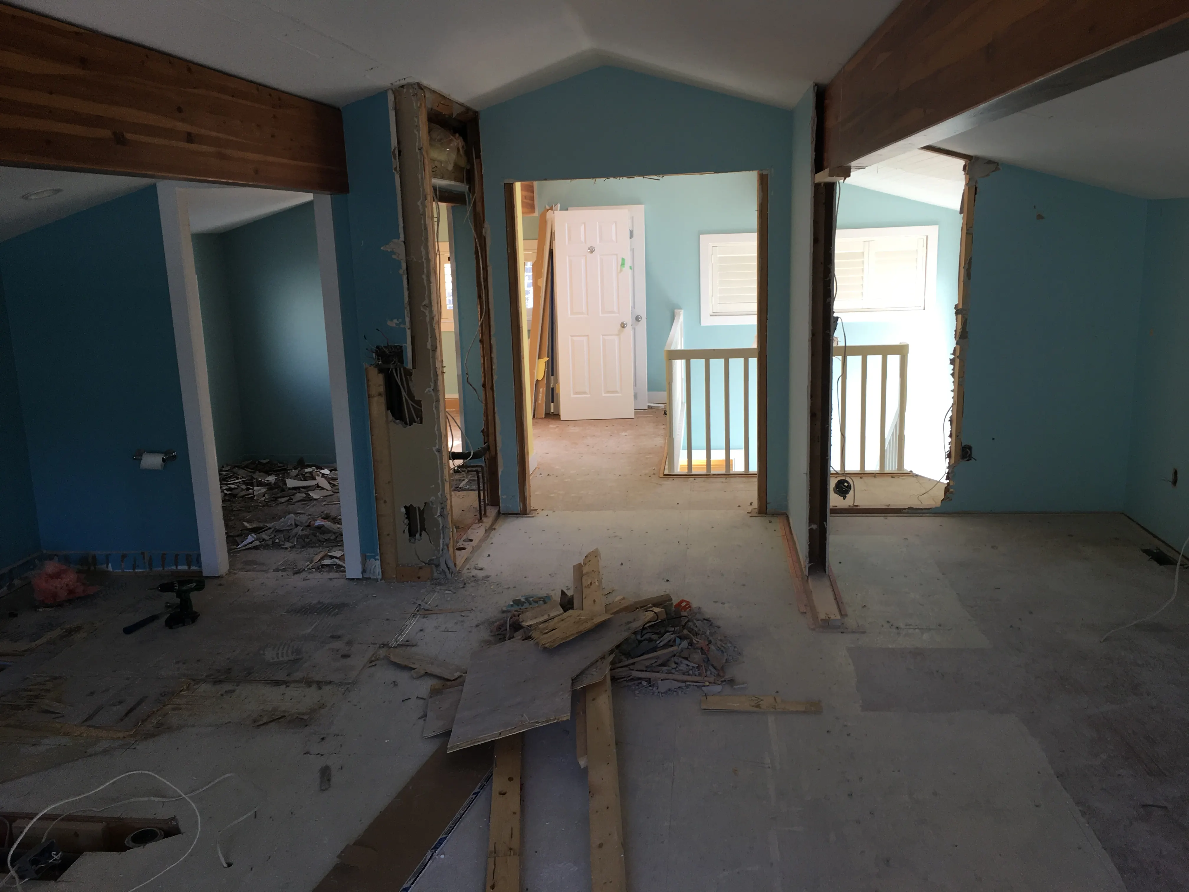 The main floor stripped back to subfloor and framing, with the home’s original dated blue walls still showing
