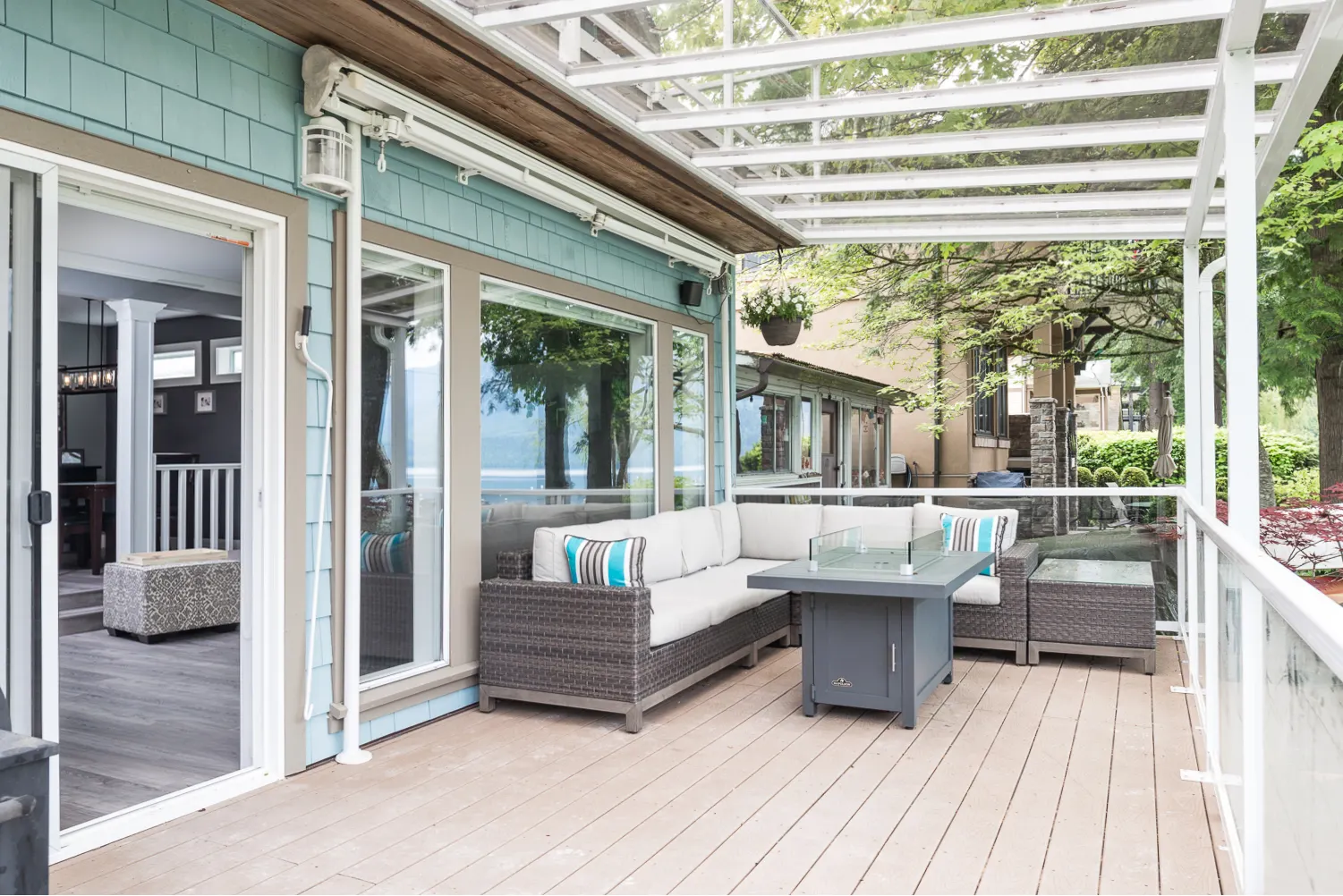 The finished covered deck with a lounge area, cedar-toned ceiling, and glass railing looking out to Cultus Lake