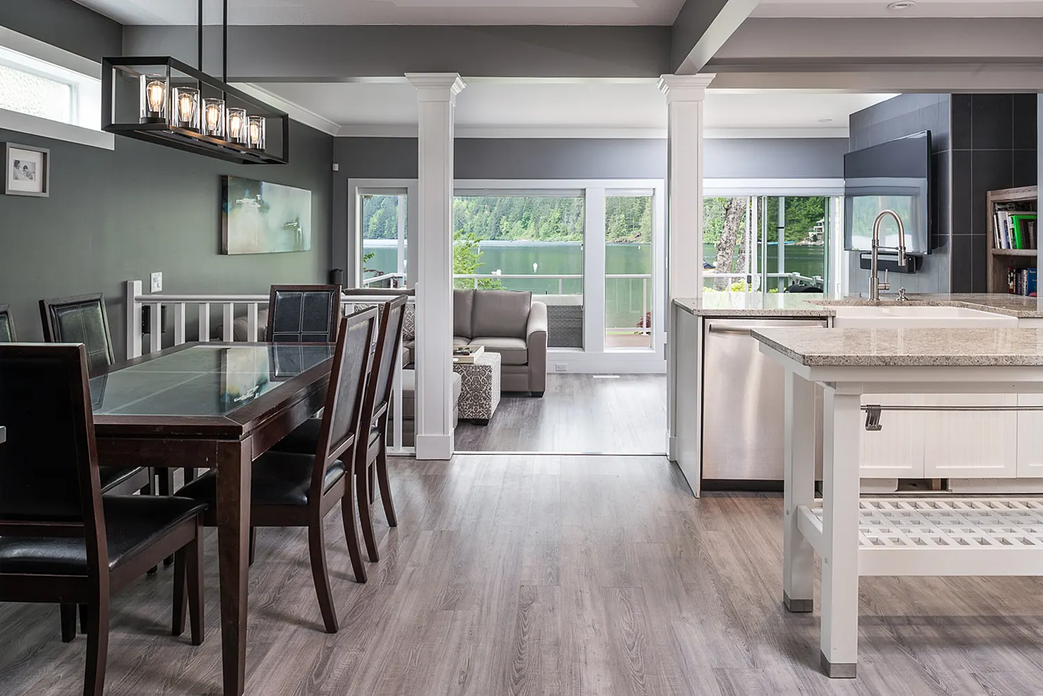 The rebuilt main floor as a bright open-concept kitchen and dining room with warm wood floors and a beamed ceiling
