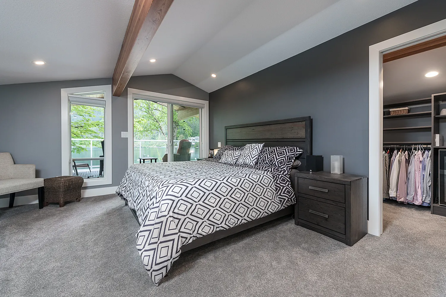 Primary bedroom with a vaulted beamed ceiling, grey walls, and windows framing the lake