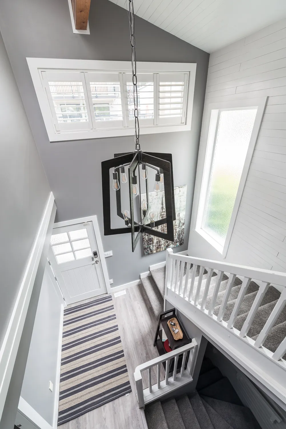 Two-storey stairwell with a modern lantern pendant, white shutters, and a striped runner