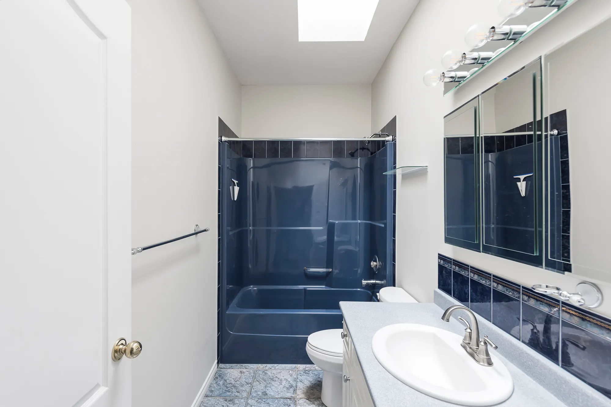 The original bathroom with a navy-blue tub-and-shower surround and dated fixtures