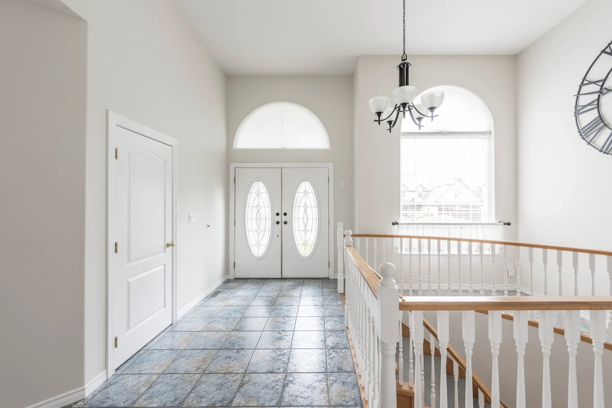 The original foyer with white spindle railings, blue-grey tile, and an oak-trimmed arched window