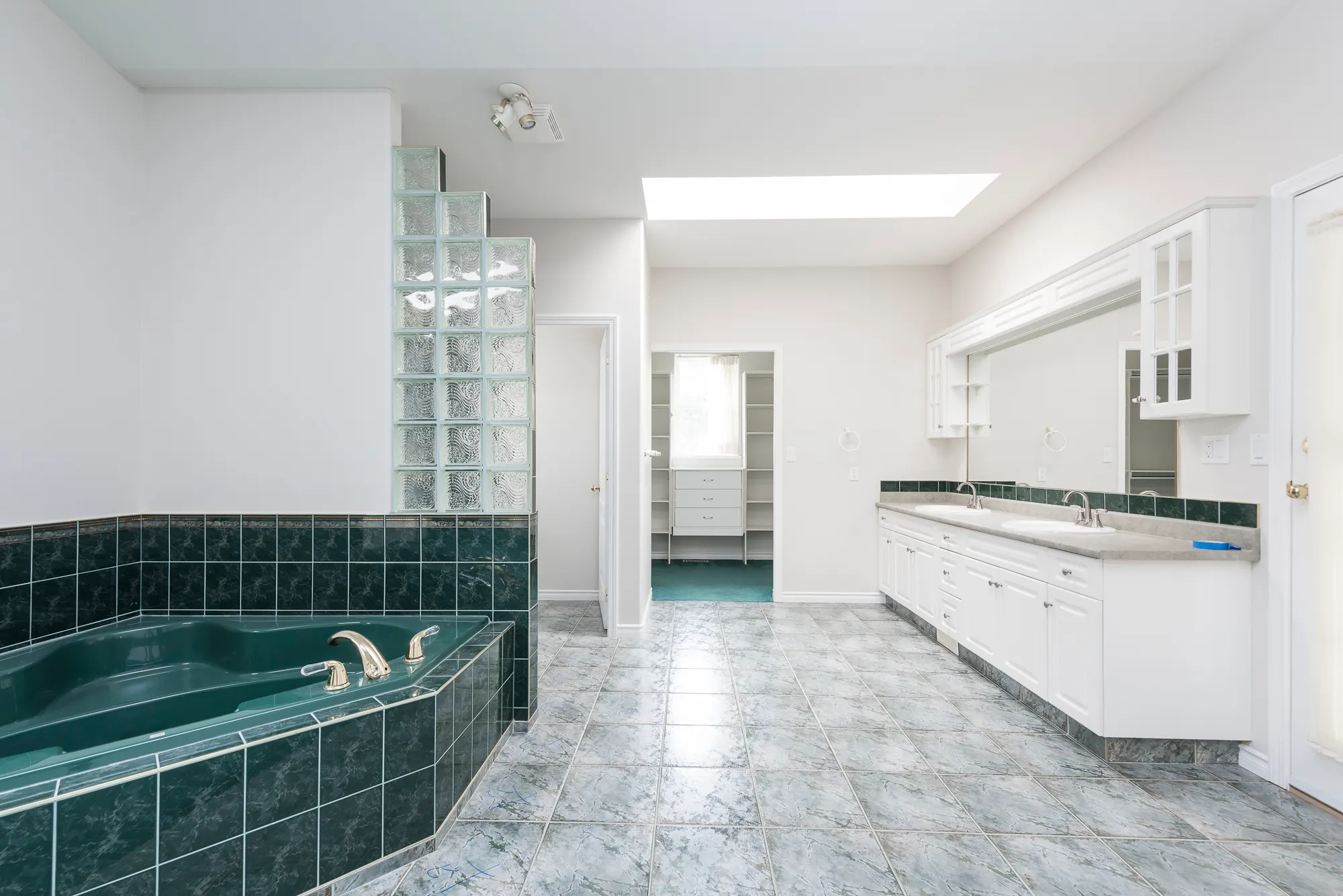 The original primary ensuite with a green-tiled corner tub, glass block, and tile floor