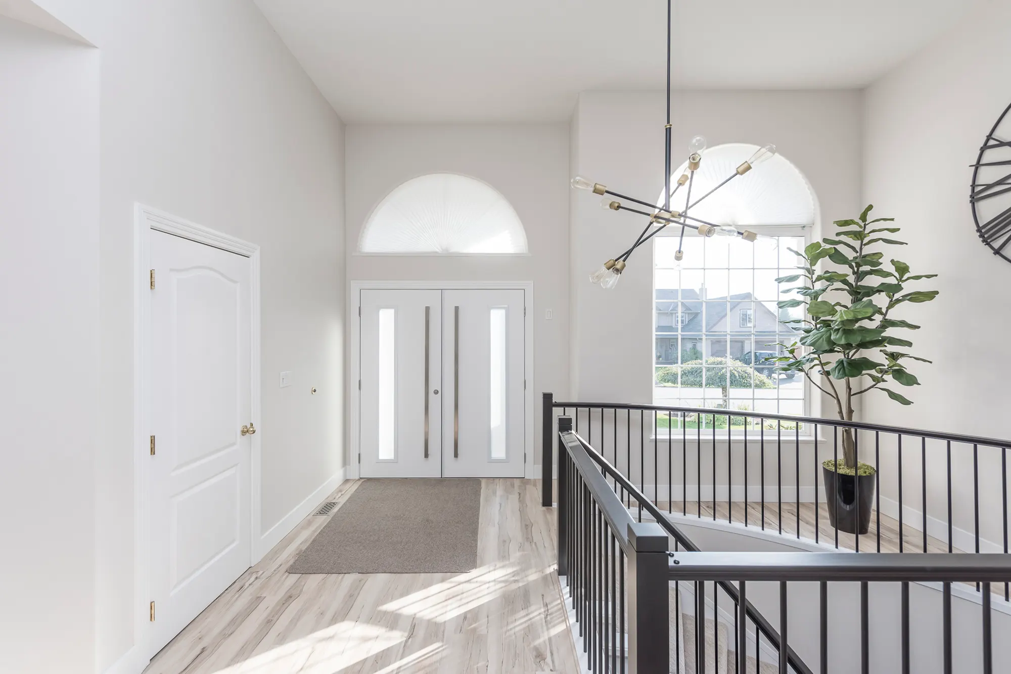 The same foyer refreshed with clean black metal railings, wood floors, and a modern chandelier