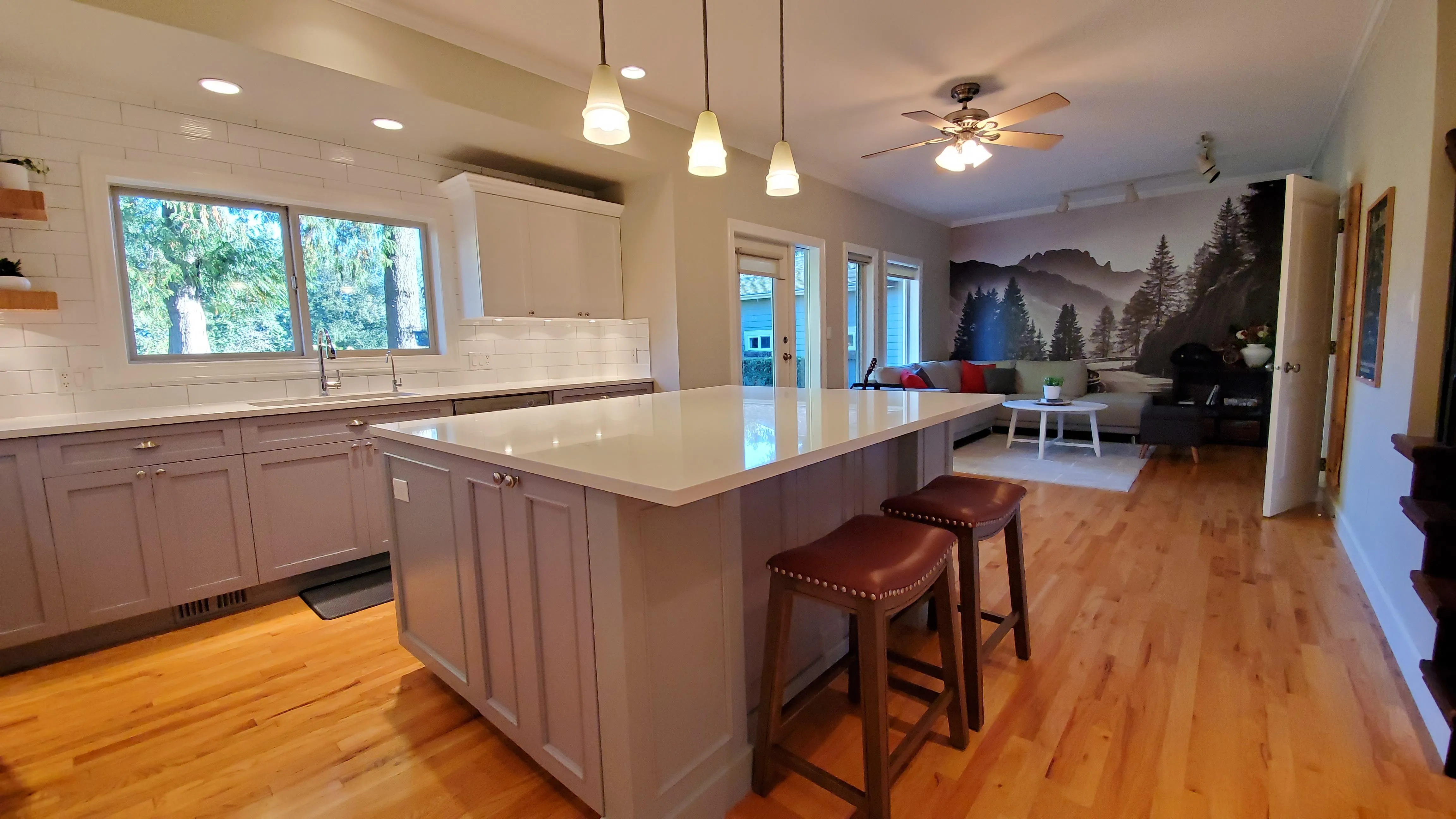 Bright open-concept kitchen and great room with a white island, wood floors, and large windows