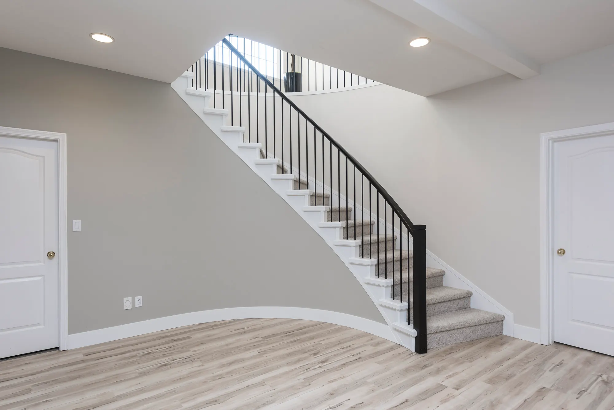 Curved staircase with white risers, black metal railing, and wood floors