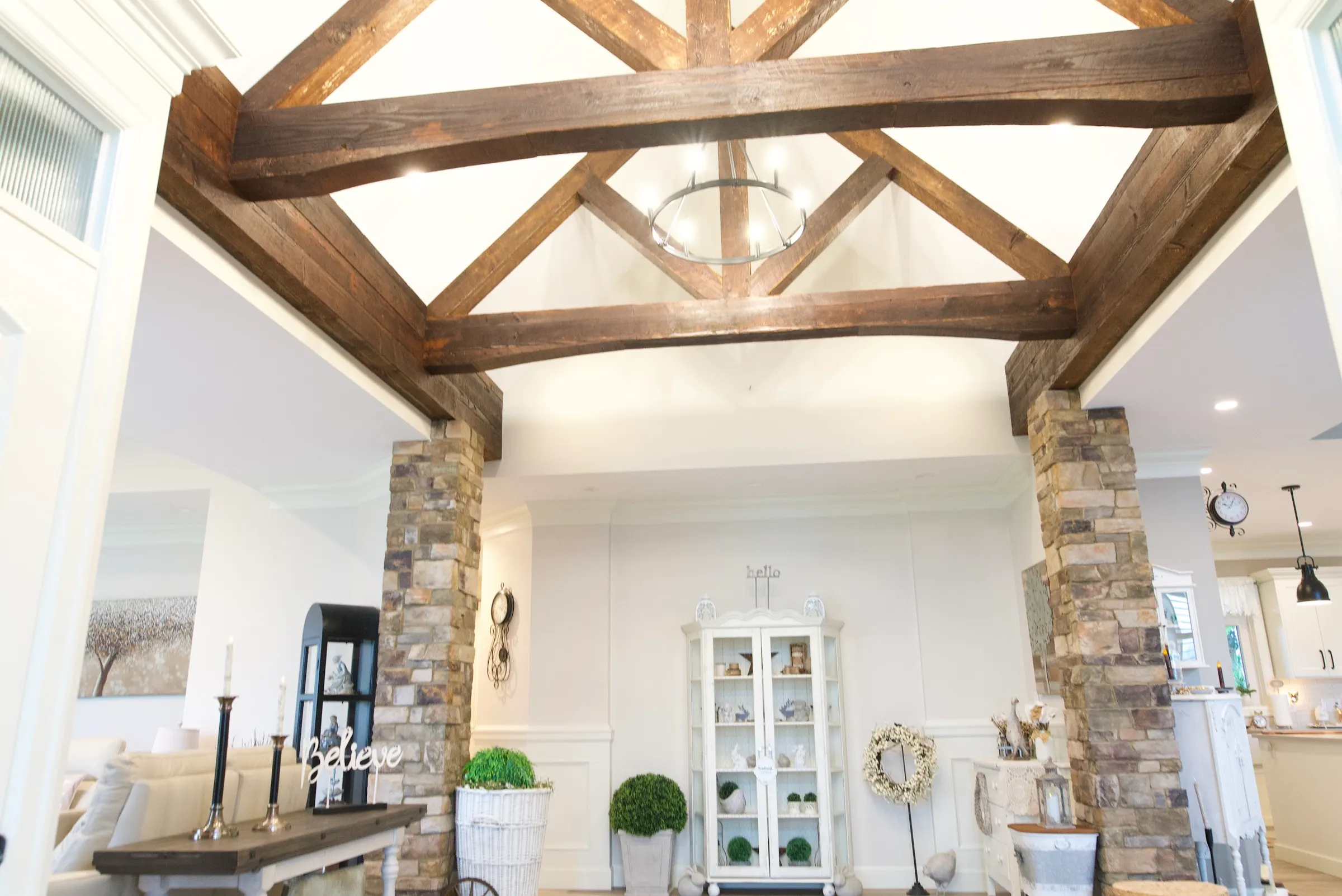 Open great room with exposed wood beams, a stacked-stone fireplace and columns, and warm plank floors