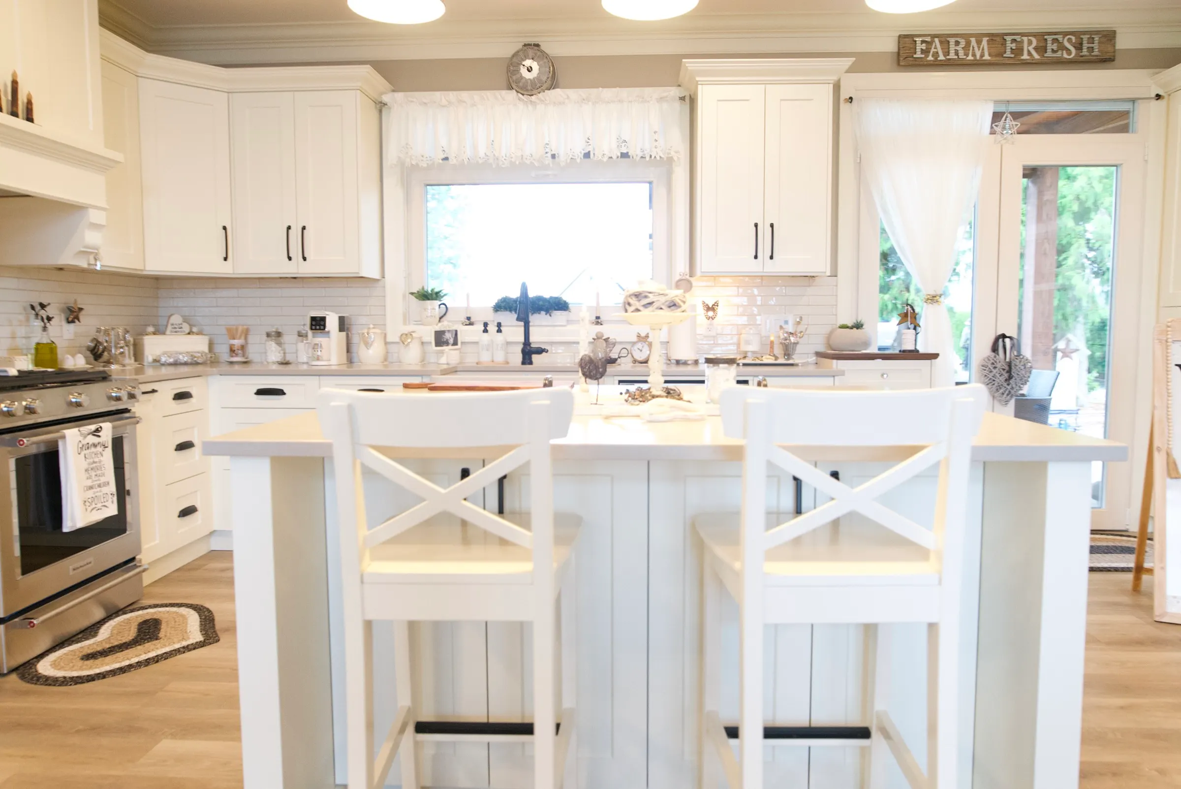 White farmhouse kitchen island with X-back stools beneath a window over the sink
