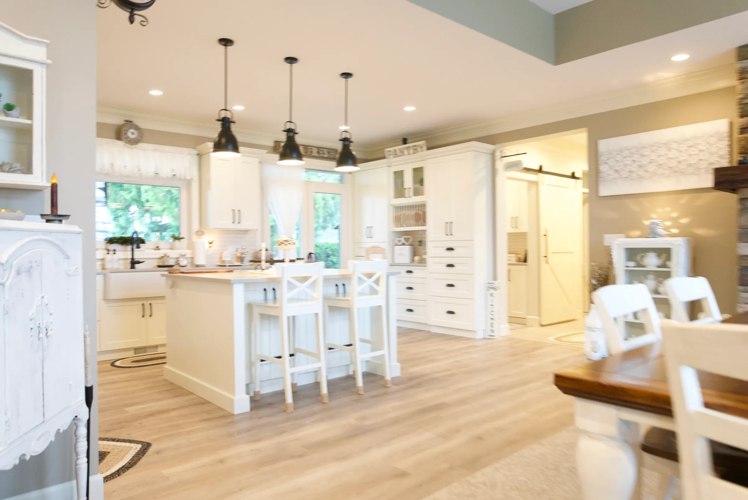 Bright open-concept kitchen with a white island, X-back stools, and black pendant lights