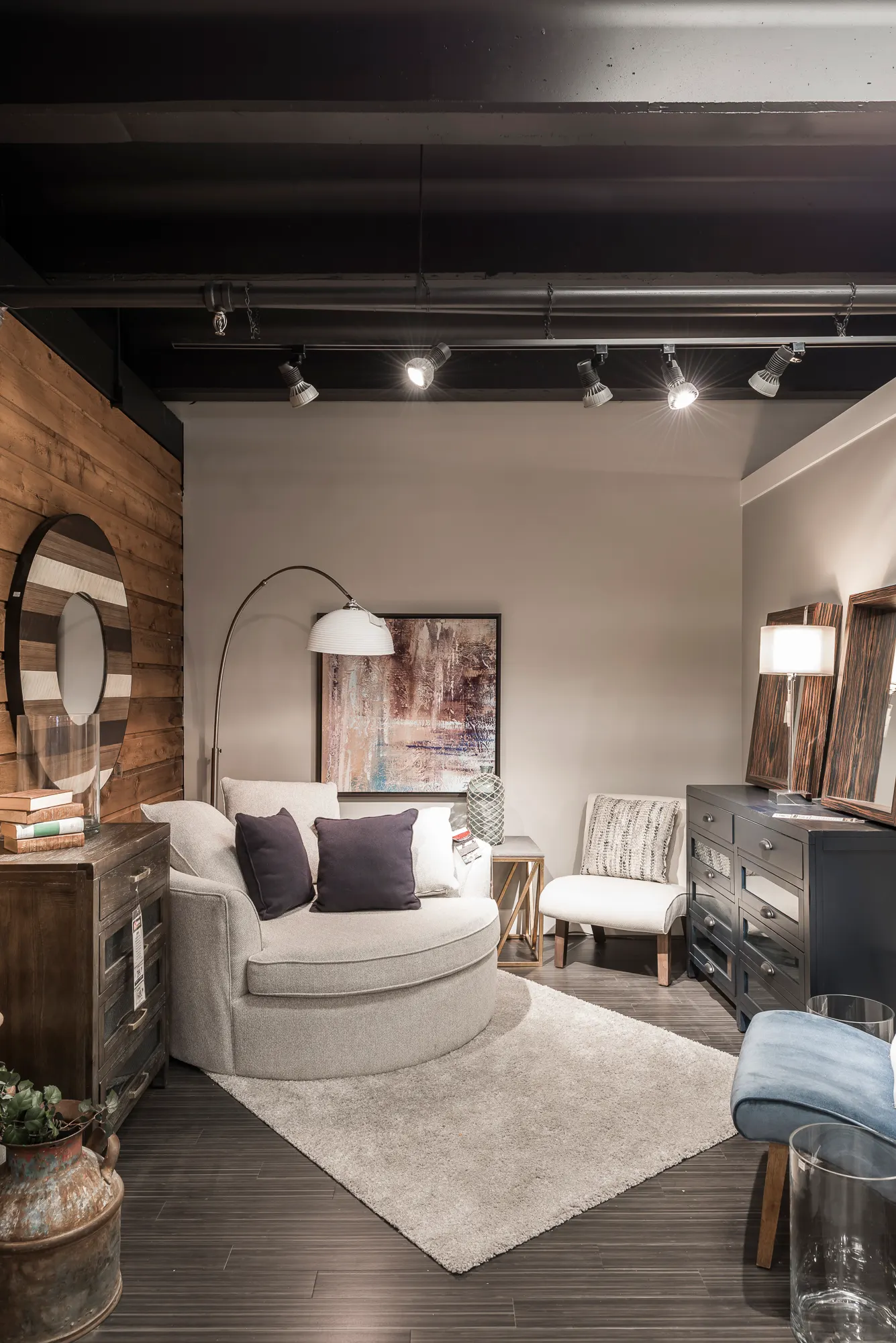 Showroom vignette with a wood accent wall, round mirror, and arc floor lamp