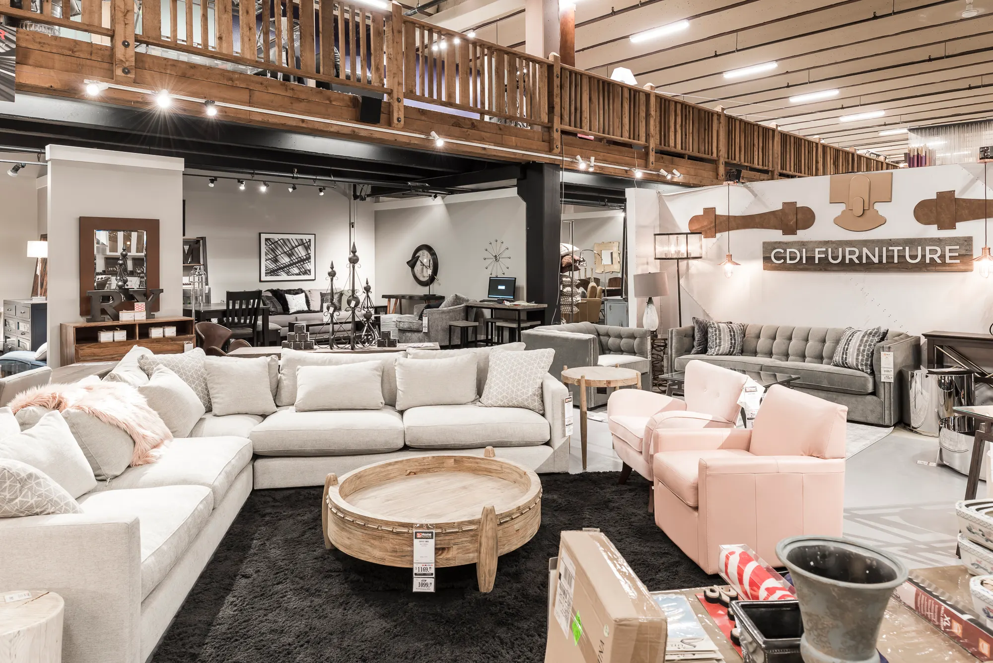 Showroom floor with sectionals and pink armchairs beneath the wood-railed mezzanine