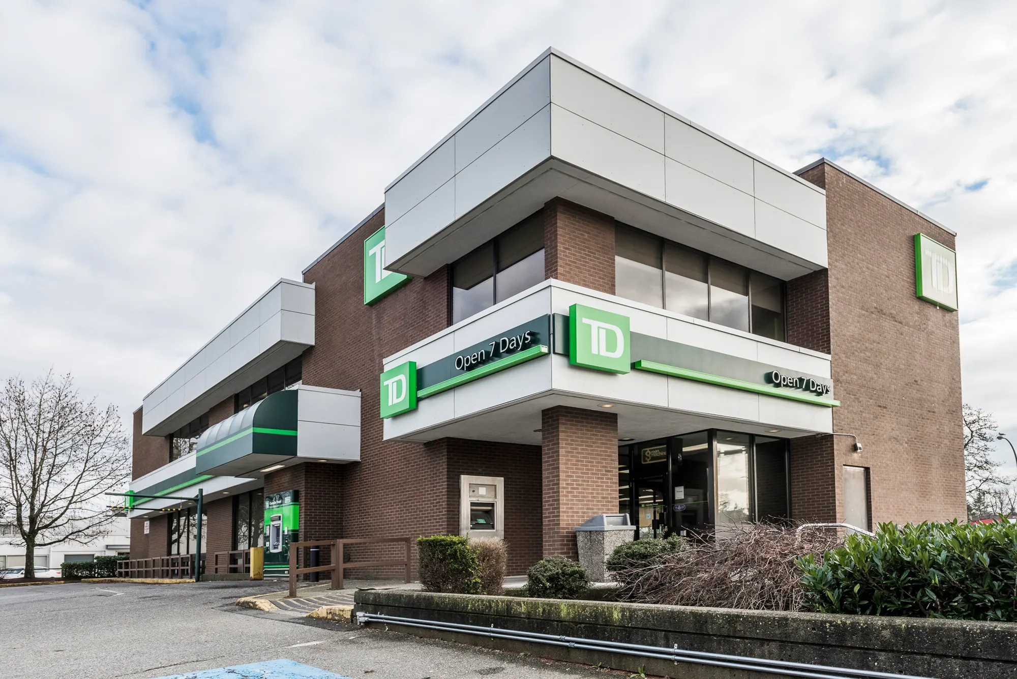 Street side of the TD Bank branch with the green Open 7 Days band and drive-up lane