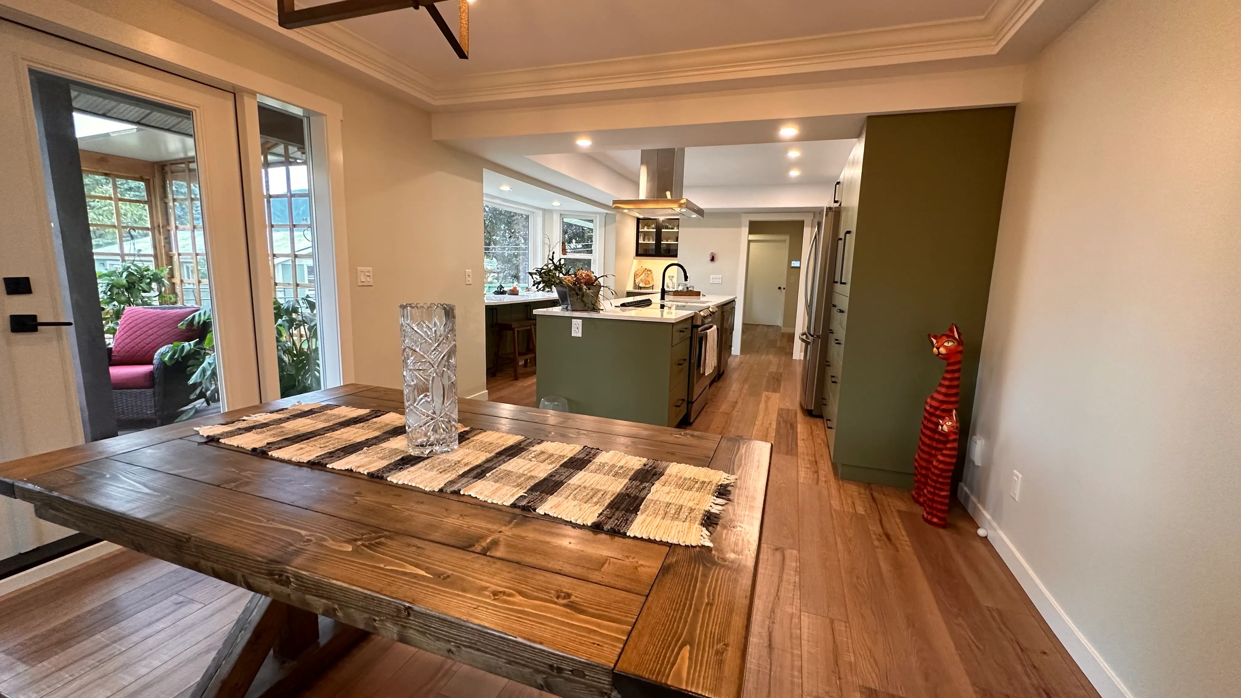 Dining area open to the kitchen with a wood table and sage-green cabinetry beyond