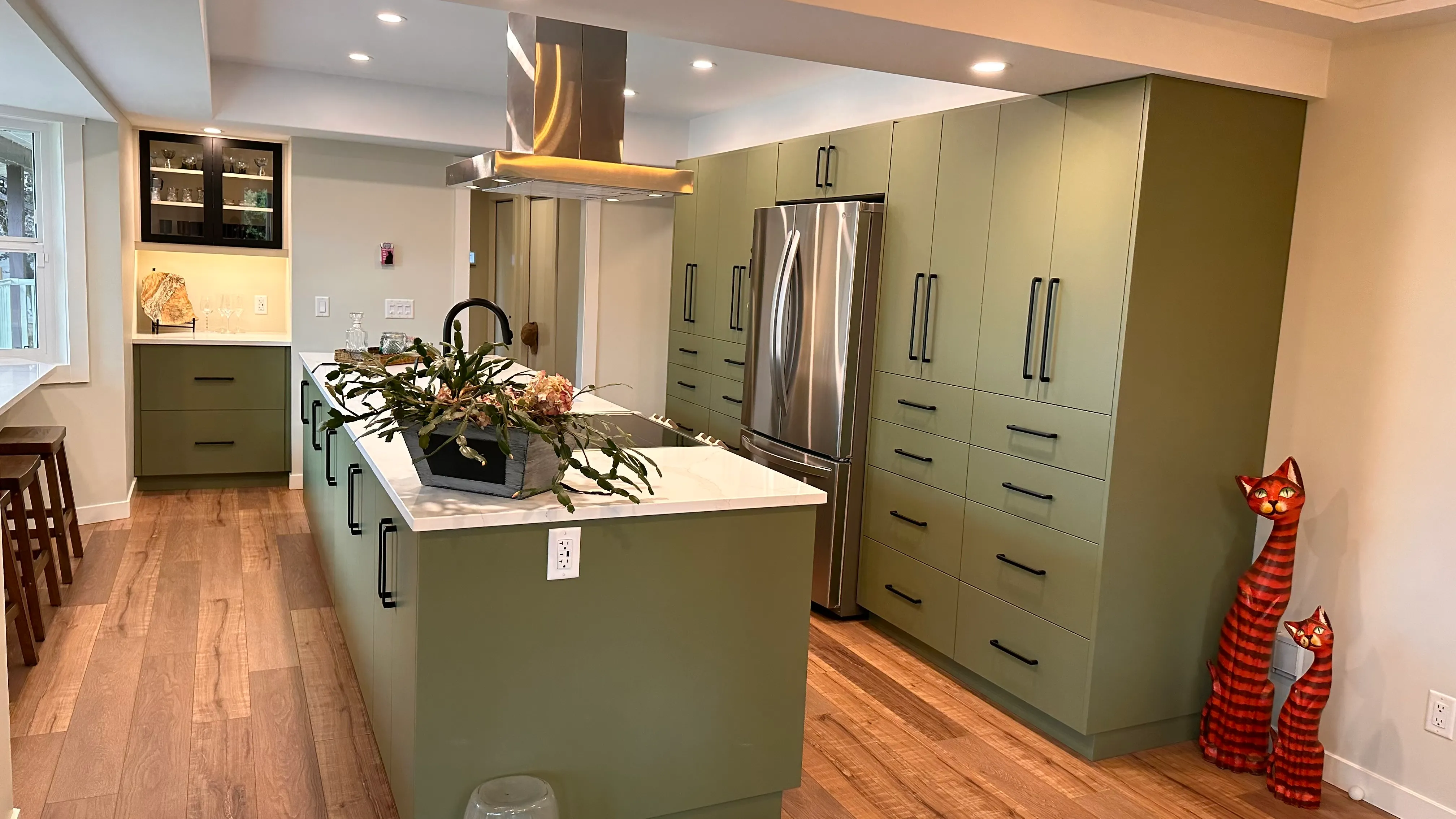 Bright sage-green kitchen with a white quartz waterfall island and wood floors after renovation