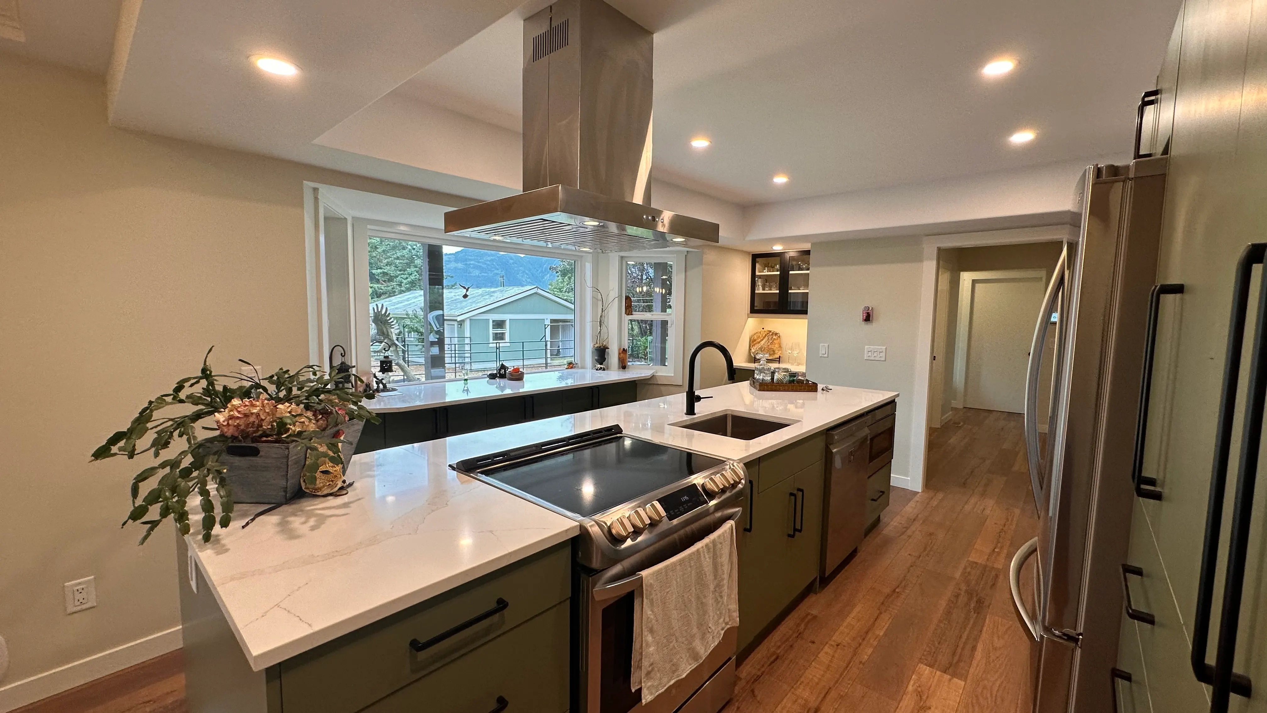 Sage-green kitchen island in white quartz beneath a statement range hood