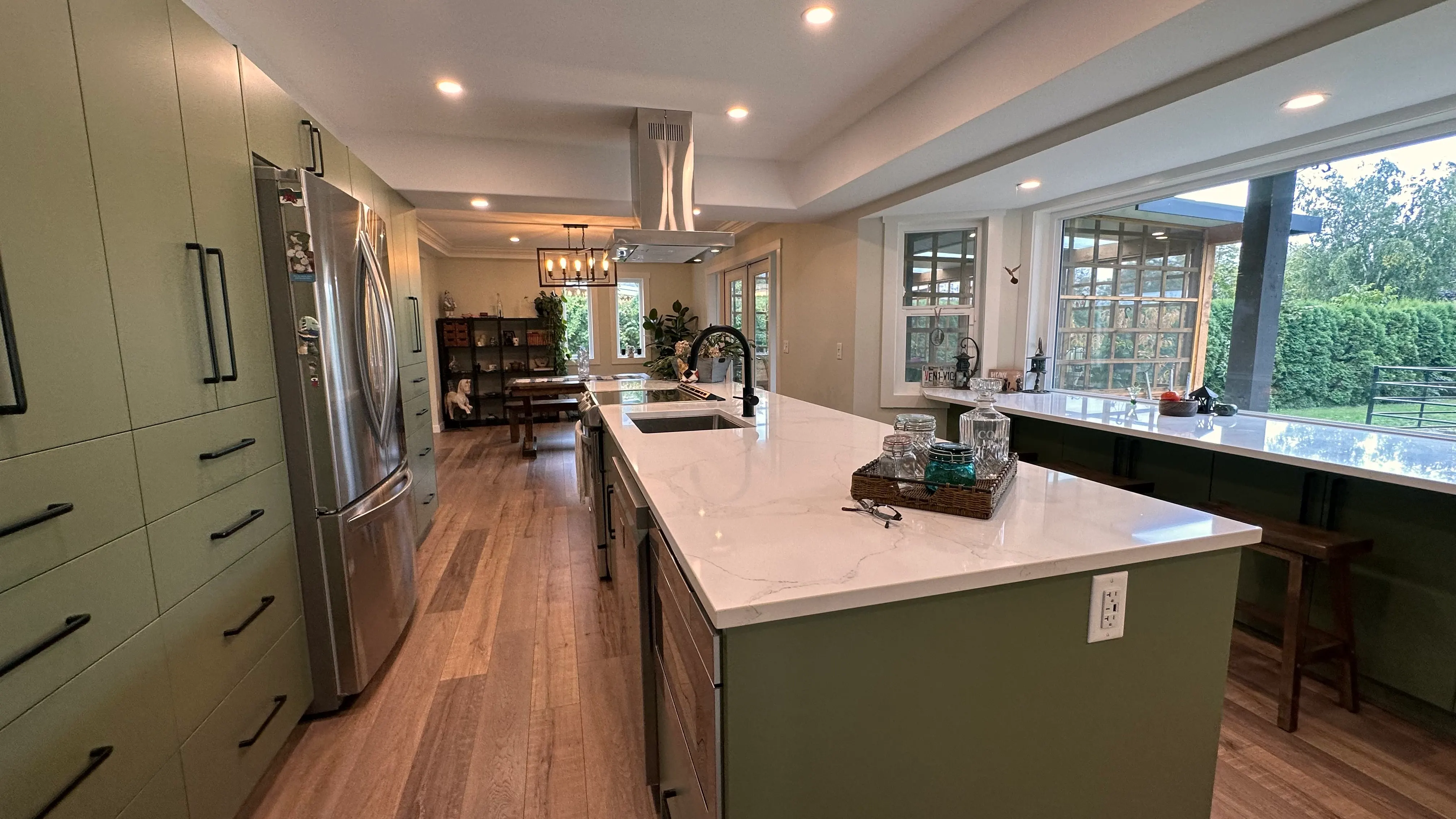 The new open kitchen with sage-green cabinetry, a white quartz waterfall island, and a statement hood