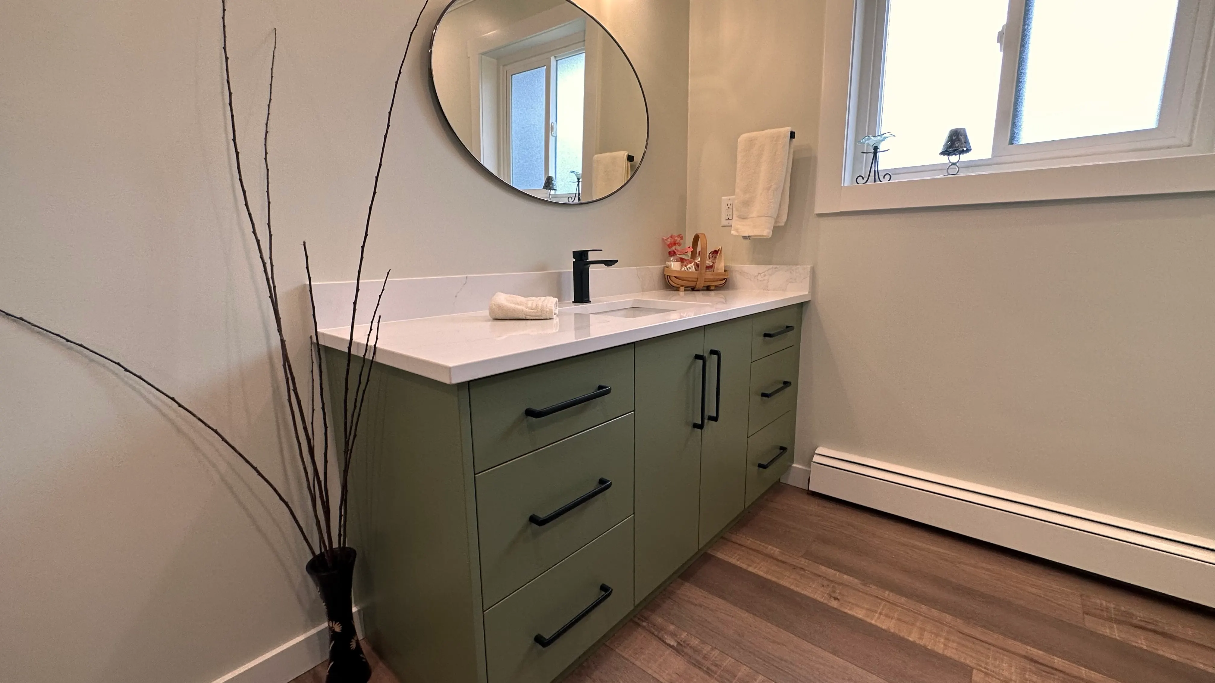 Bathroom vanity in sage green with a round mirror and black fixtures