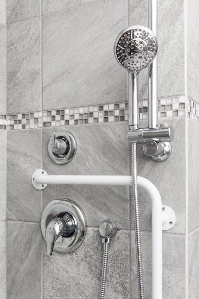 Accessible shower with grab bar, handheld showerhead, and lever-style faucet in a modern tiled bathroom