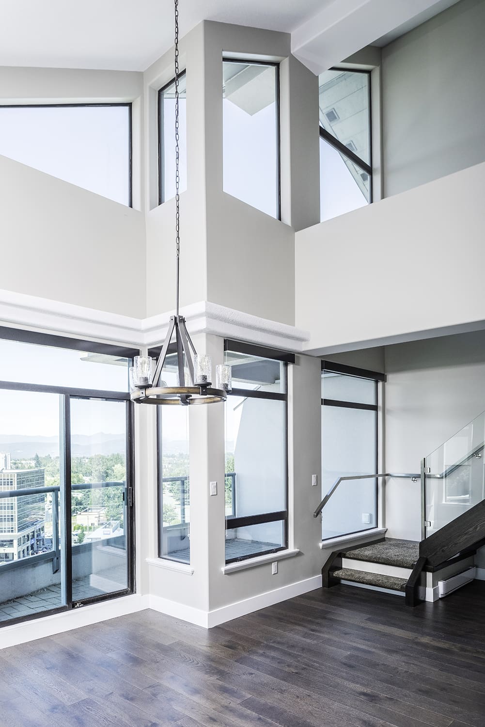 Modern high-rise interior with double-height ceilings, crisp professionally painted walls, glass staircase railing, and natural light highlighting premium architectural finishes