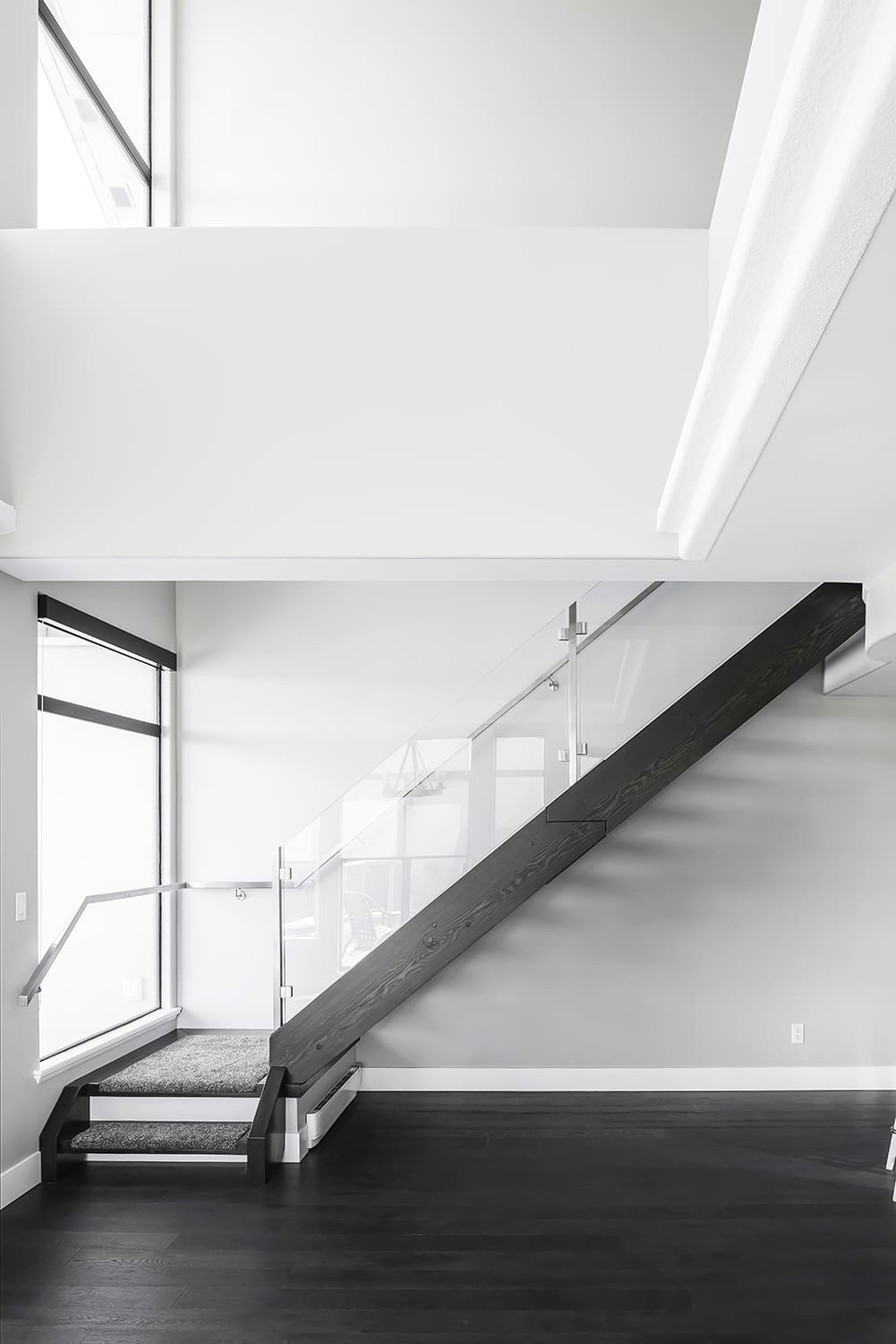 Modern staircase with dark wood stringers, glass railing, and crisp white professionally painted walls showcasing clean lines and architectural precision in Abbotsford home renovation