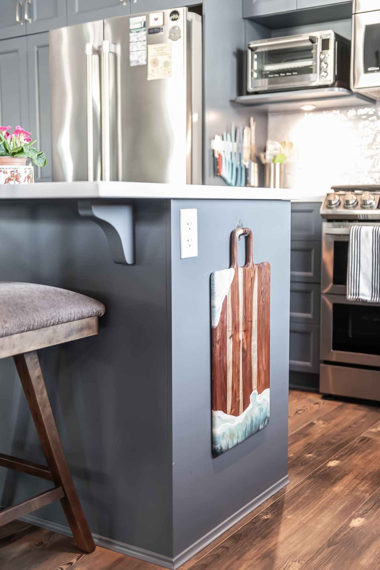 Custom handcrafted resin and wood cutting board hanging on blue kitchen island with stainless steel appliances and hardwood flooring