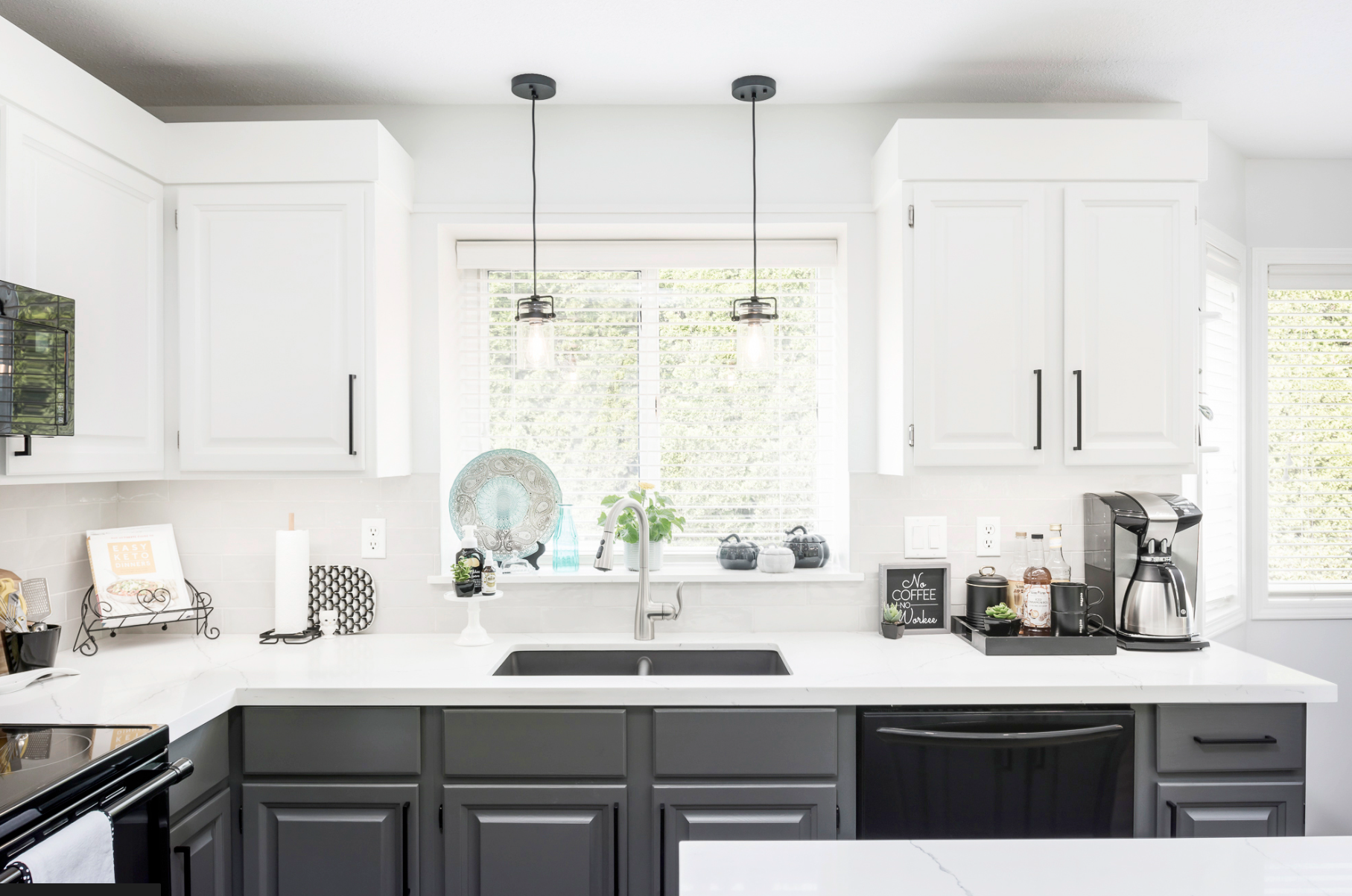 Two-tone kitchen renovation in Chilliwack featuring white upper cabinets, dark charcoal lower cabinets, white quartz countertops, pendant lighting, and natural light by Master Painting and Renovations