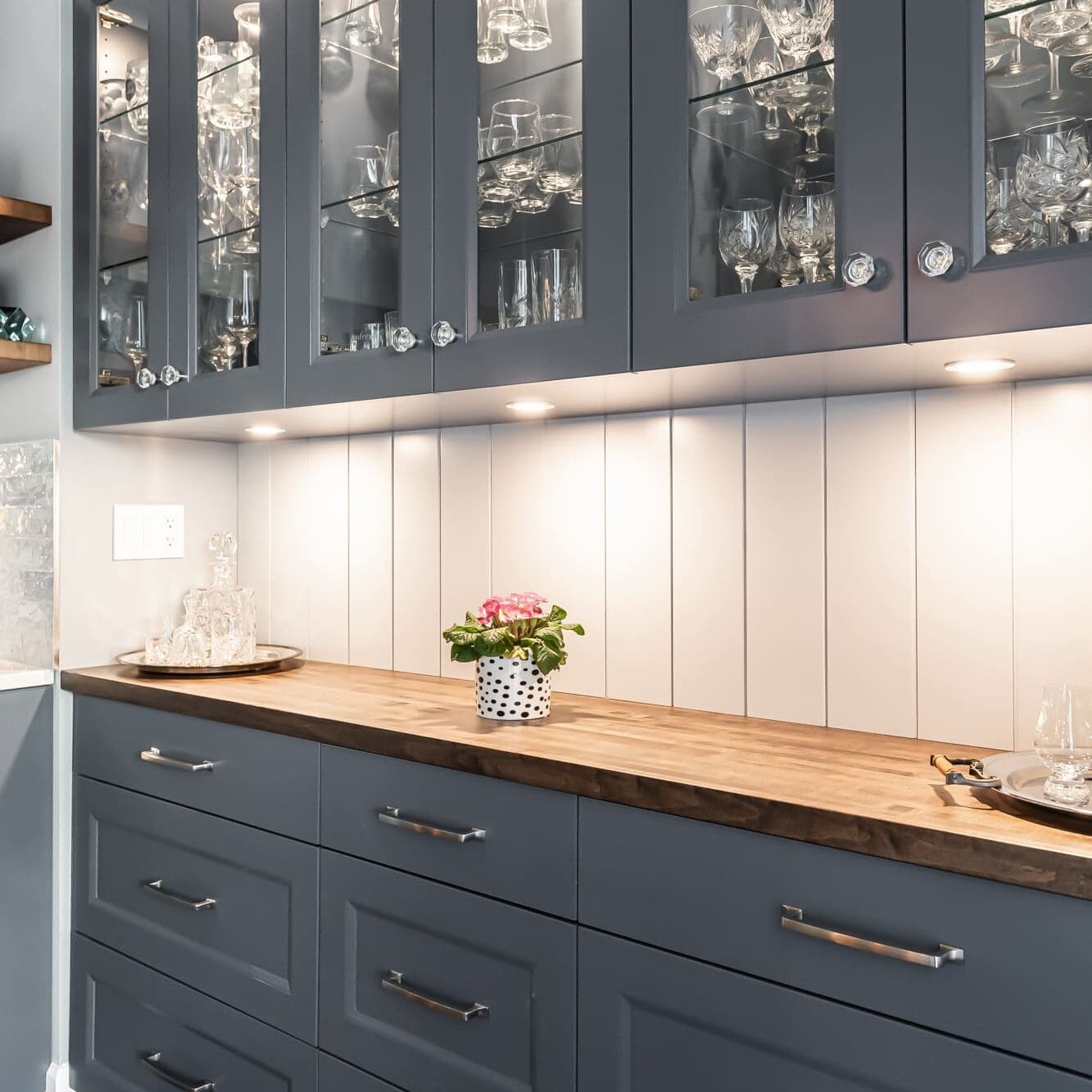 Dark blue kitchen cabinets with glass doors displaying crystal glassware, butcher block countertop, and under-cabinet lighting in a Chilliwack home
