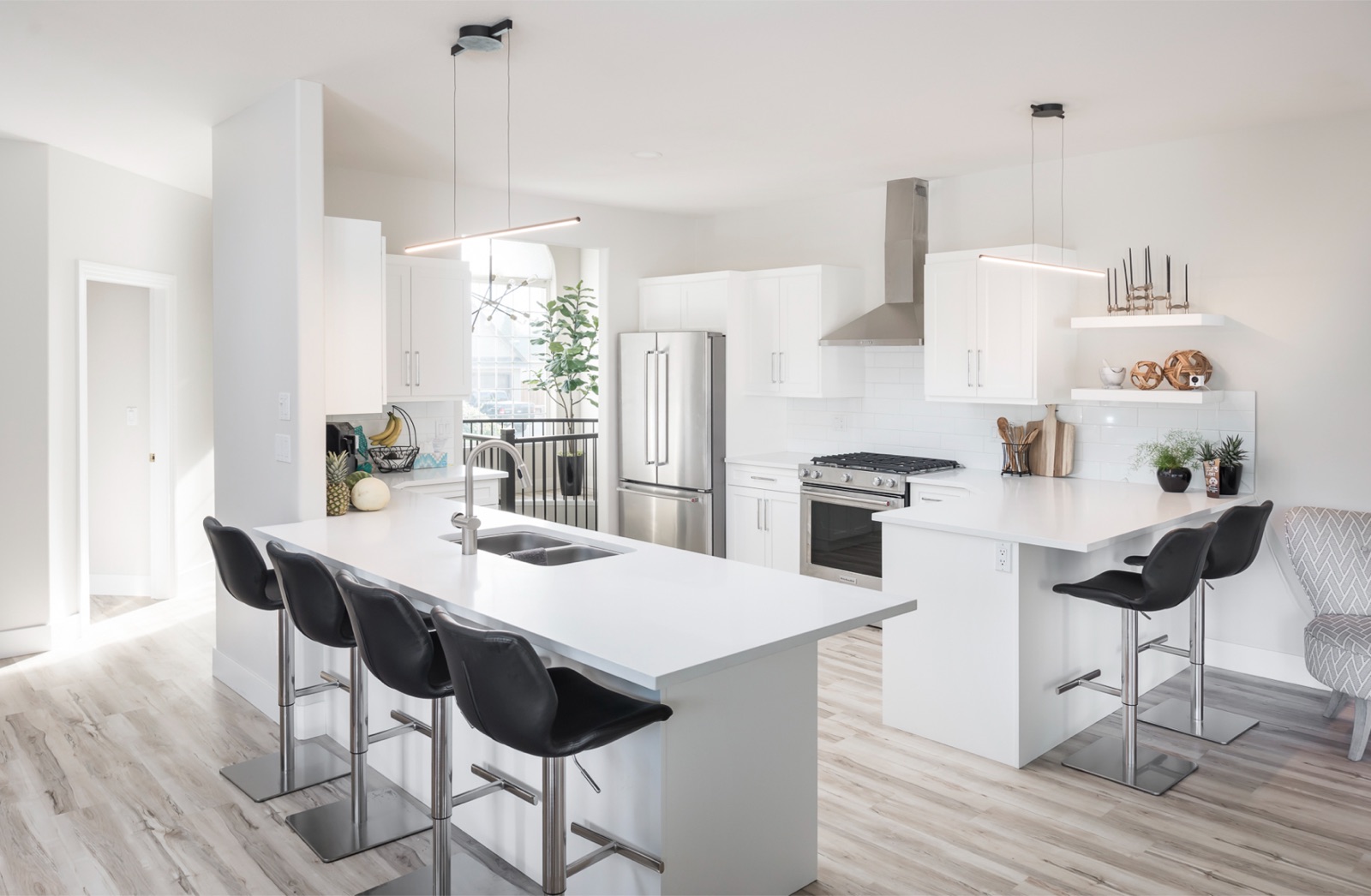 Modern white kitchen renovation in Chilliwack by Master Painting and Renovations featuring white quartz island countertop, black bar stools, stainless steel appliances, and pendant lighting