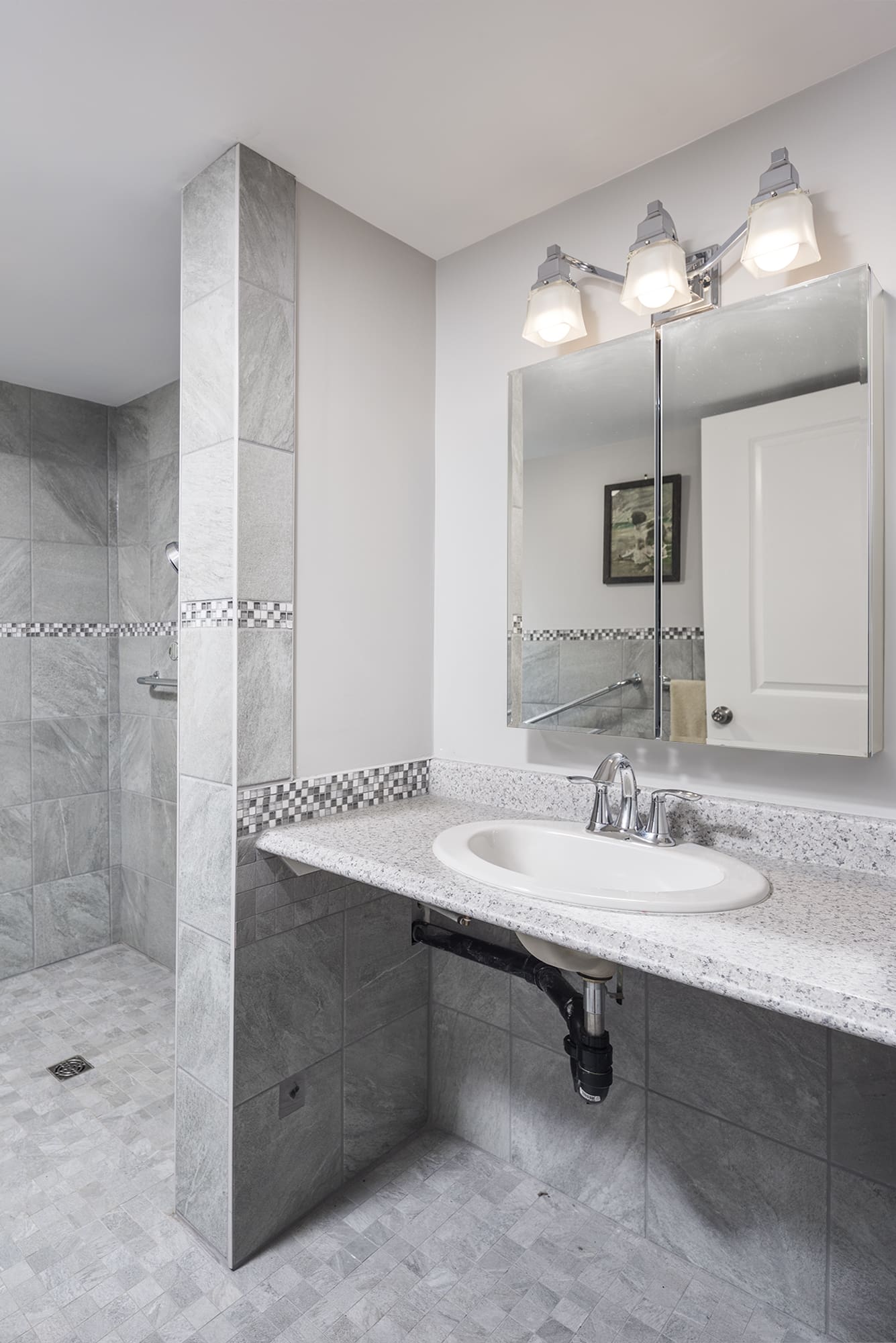 Accessible bathroom with roll-under sink, open shower design, grab bars, and bright vanity lighting for safe aging in place