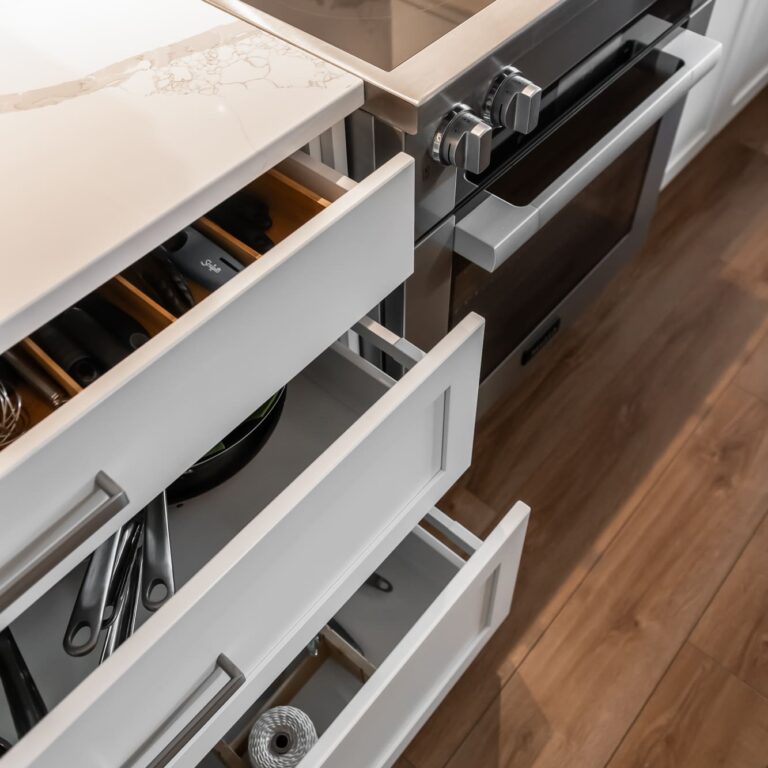 Modern kitchen drawers with organized storage beside a sleek induction cooktop and stainless steel oven, featuring clean white cabinetry and marble-look countertops
