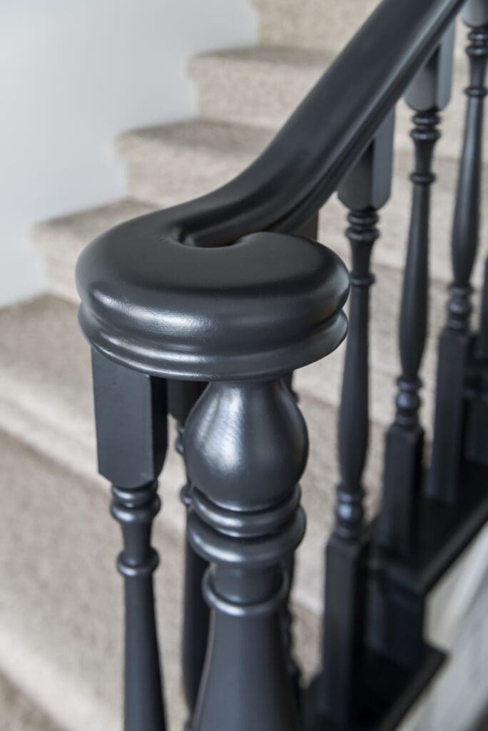 Close-up of black satin-finish staircase railing with traditional spindles and beige carpeted stairs in a renovated Chilliwack home.