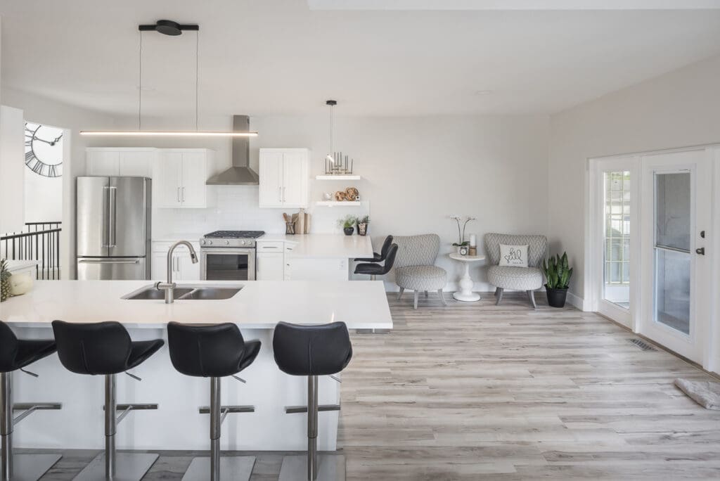 Open-concept kitchen with white cabinetry, stainless steel appliances, and seamless light-toned flooring extending into a bright seating area — demonstrating visual continuity and space-enhancing layout.