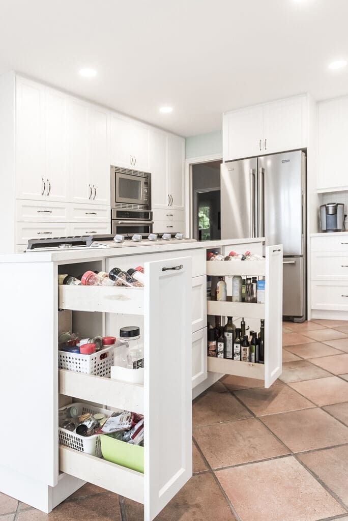 White kitchen island with open pull-out pantry drawers organized with spices, oils, and condiments — showcasing smart interior storage solutions for small kitchens.